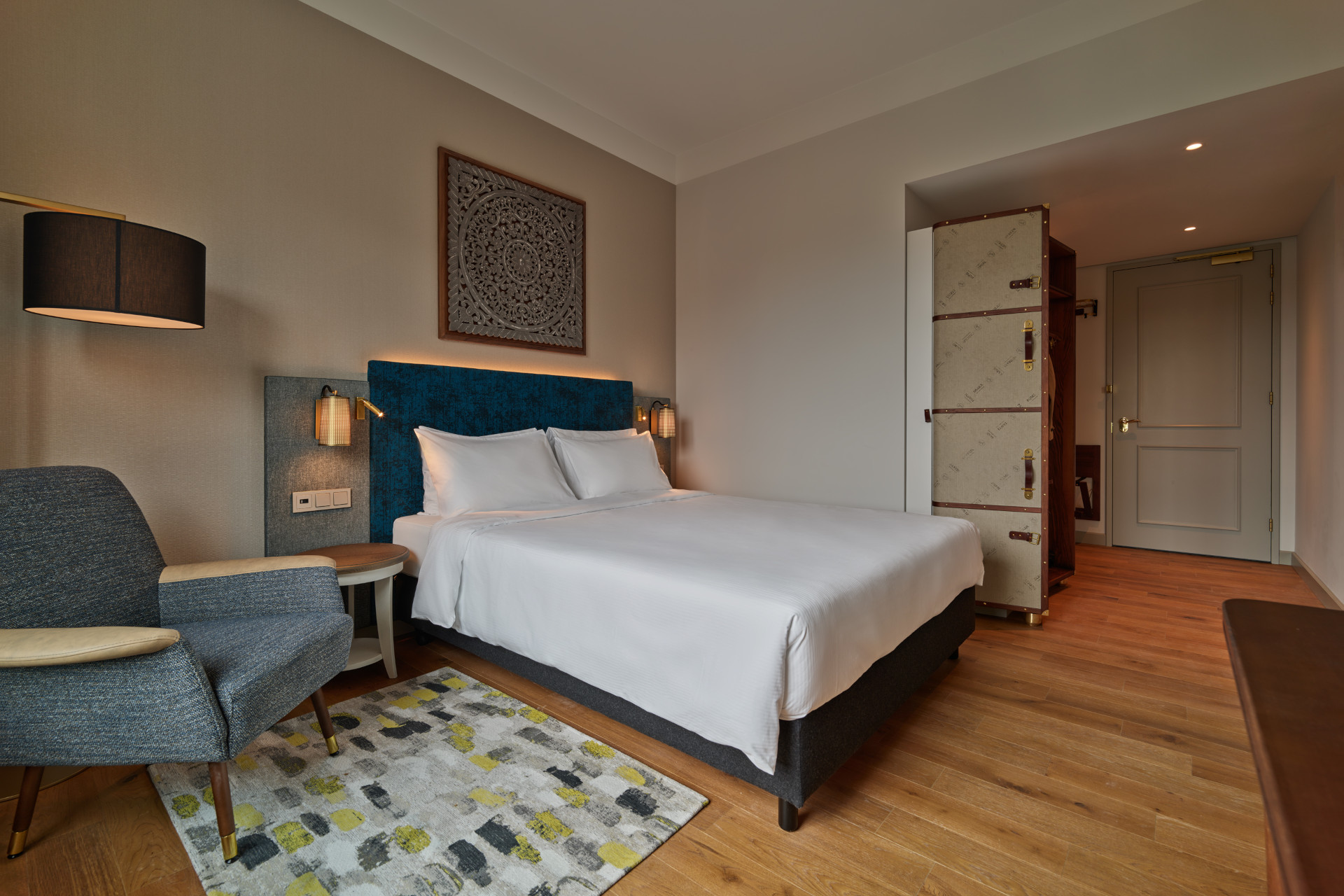 Comfortable queen bedroom at voco The Hague with USB/USB-C charging, minifridge, and natural light.